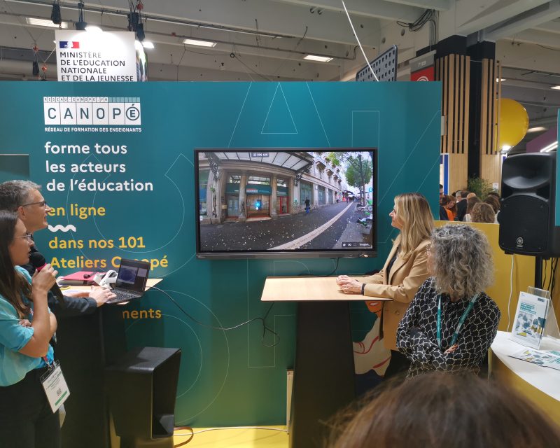 Stand de Réseau Canopé au salon Educatech lors de la présentation d'un projet. Une personne à un pupitre commente une vidéo de présentation du projet Marseille en grand de la direction territoriale Réseau Canopé de Provence-Alpes-Côte d'Azur