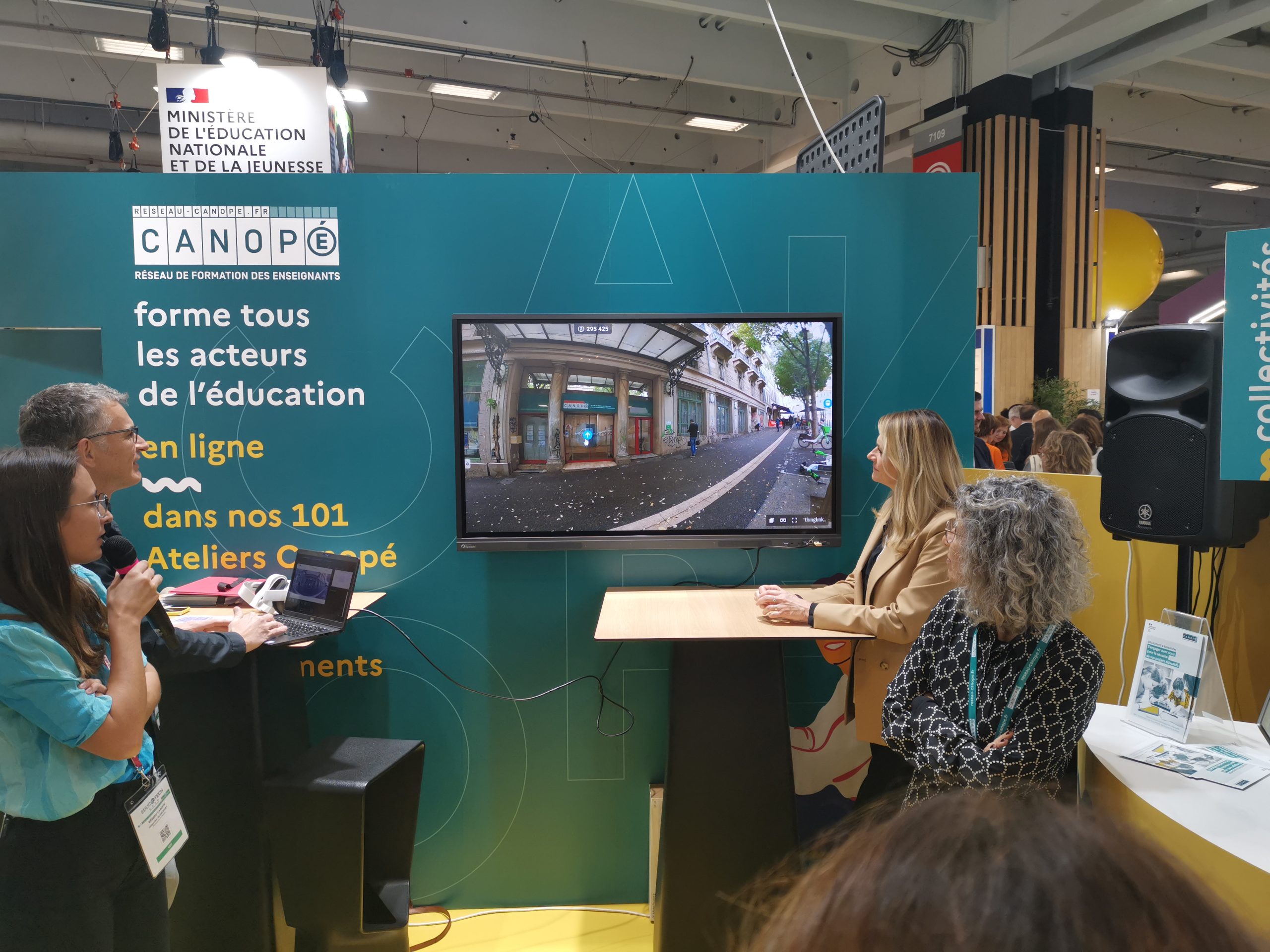 Stand de Réseau Canopé au salon Educatech lors de la présentation d'un projet. Une personne à un pupitre commente une vidéo de présentation du projet Marseille en grand de la direction territoriale Réseau Canopé de Provence-Alpes-Côte d'Azur