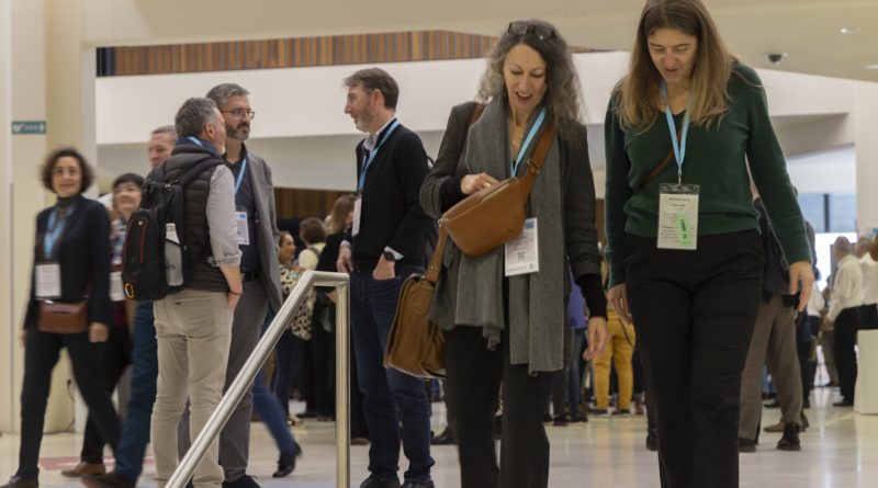 Groupe de participants se déplaçant et échangeant dans le hall d’un événement, portant des badges autour du cou.
