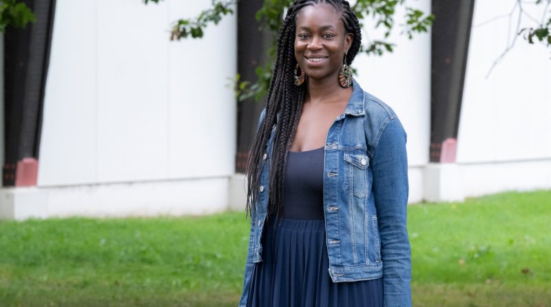 jeune femme souriante vêtue d’une robe de couleur bleu et d’une veste en jean