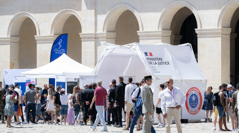 Une foule de visiteurs, dont des civils et des militaires en uniforme, se presse autour de du stand du ministère de la Justice et de l’administration pénitentiaire installé dans la cour d’honneur de l’Hôtel des Invalides à Paris en 2022. En arrière-plan, la façade du Musée de l’Armée avec ses arches et son inscription dorée.