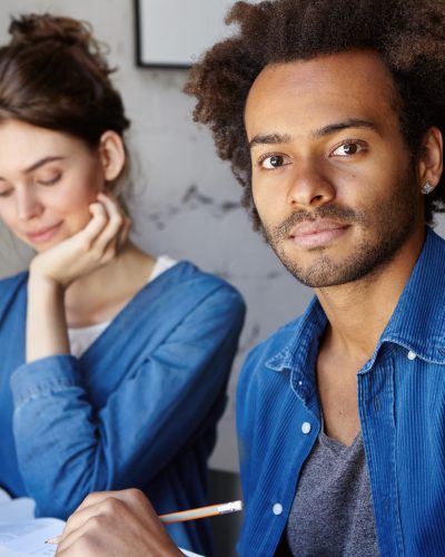 deux étudiants, une jeune femme et un jeune homme, vêtus dans un style décontracté, prennent des notes pendant un cours.