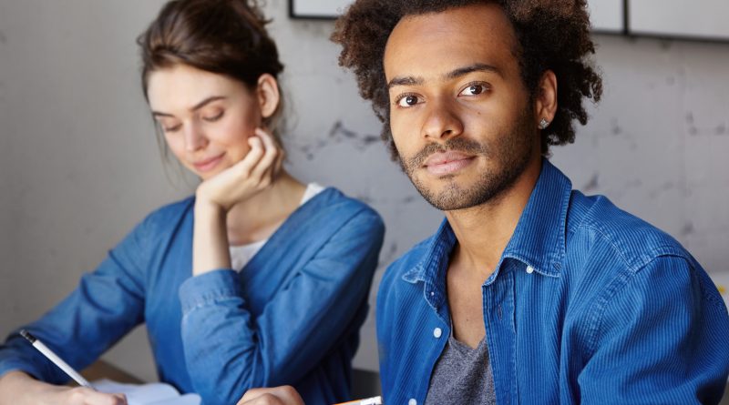 deux étudiants, une jeune femme et un jeune homme, vêtus dans un style décontracté, prennent des notes pendant un cours.