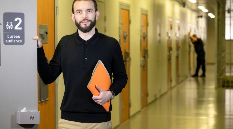 Au premier plan : un homme tenant dossier papier. Il ouvre une porte sur laquelle est écrit bureau d’audience. Au second plan, un couloir de prison, les portes des cellules sont fermées. Au fond, on distingue un surveillant pénitentiaire vérifiant une porte de cellule.