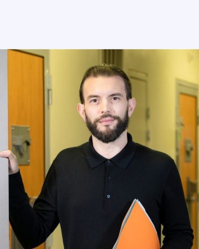 Au premier plan : un homme tenant dossier papier. Il ouvre une porte sur laquelle est écrit bureau d’audience. Au second plan, un couloir de prison, les portes des cellules sont fermées. Au fond, on distingue un surveillant pénitentiaire vérifiant une porte de cellule.